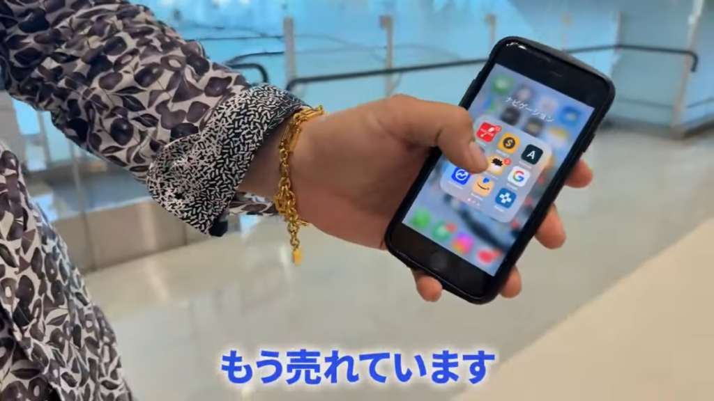 物販スクール「物販ONE」受講生の阿部さんが、仕入れ中にスマホのAmazon管理画面を見て商品が売れたことを知り、笑顔になる動画のスクリーンショット。効率的な物販の様子。